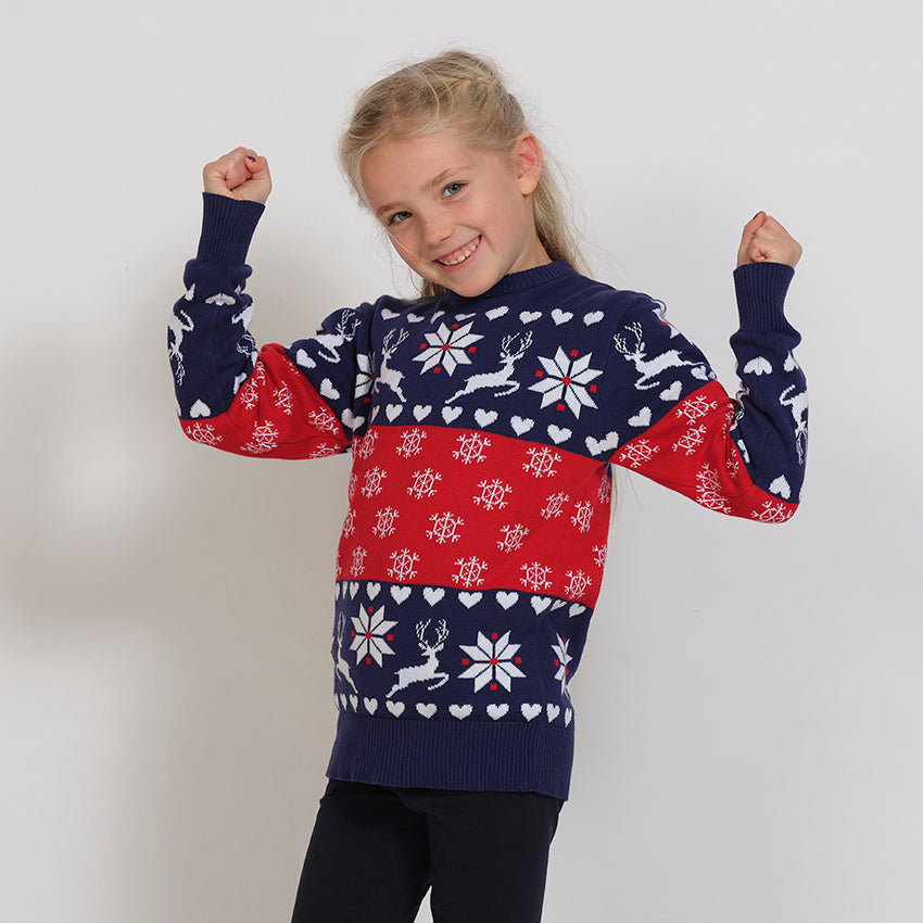 Ett barn i röd och blå jultröja med snöflingor och renar.